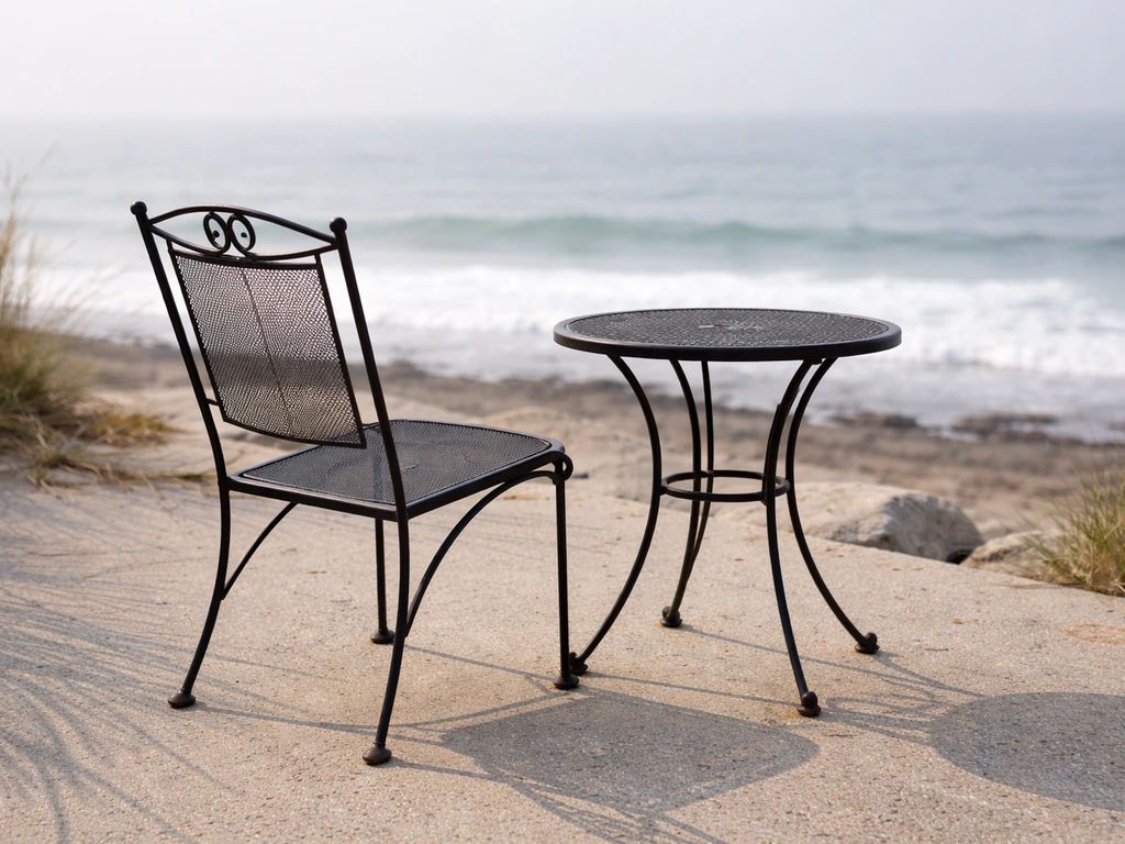 Outdoor powder-coated patio chair near the coast with subtle early rust at joints and edges.